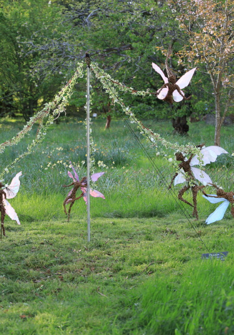 A group of fairies in the grass near a tree.